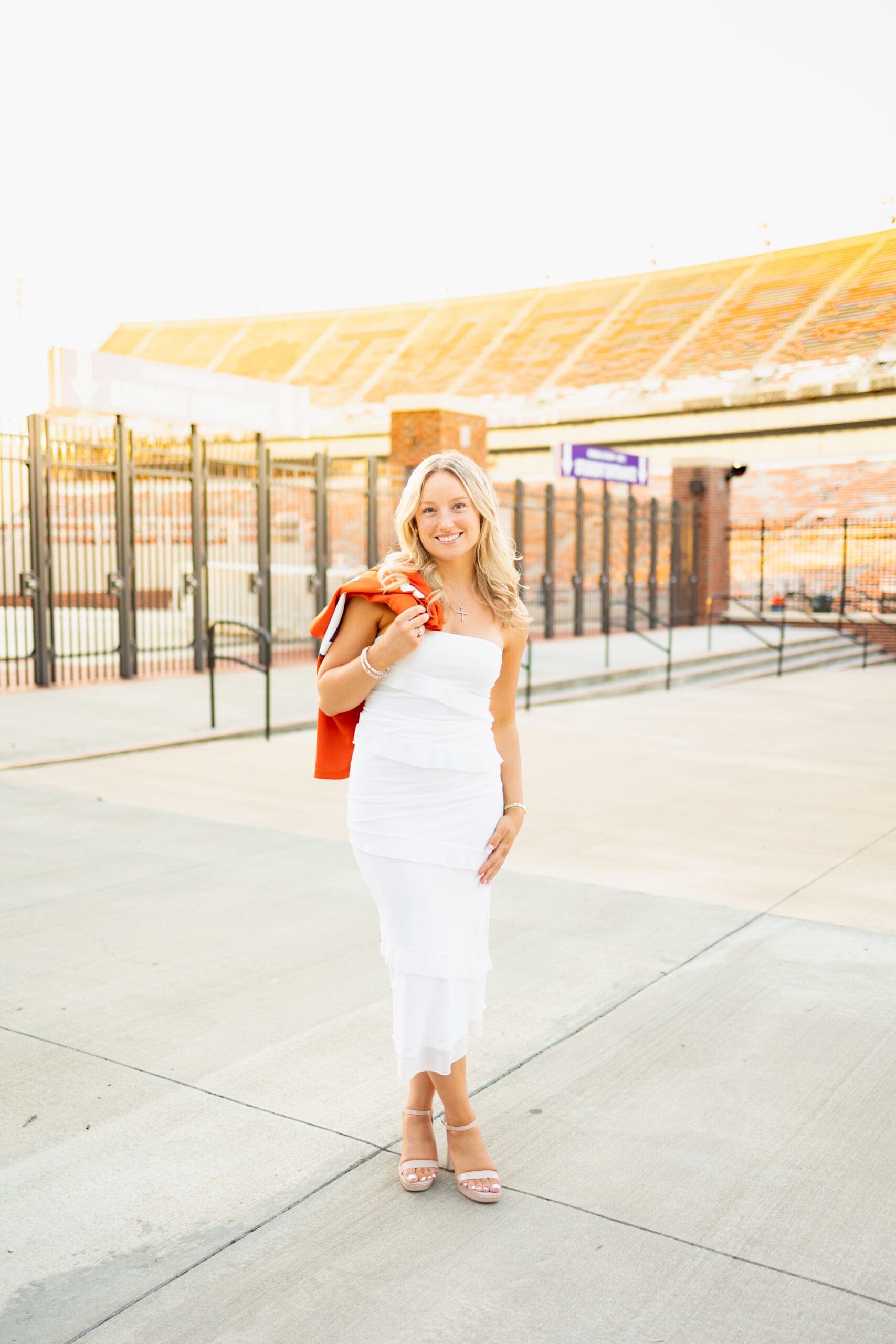 clemson university senior in white dress with orange jersey in front of football stadium