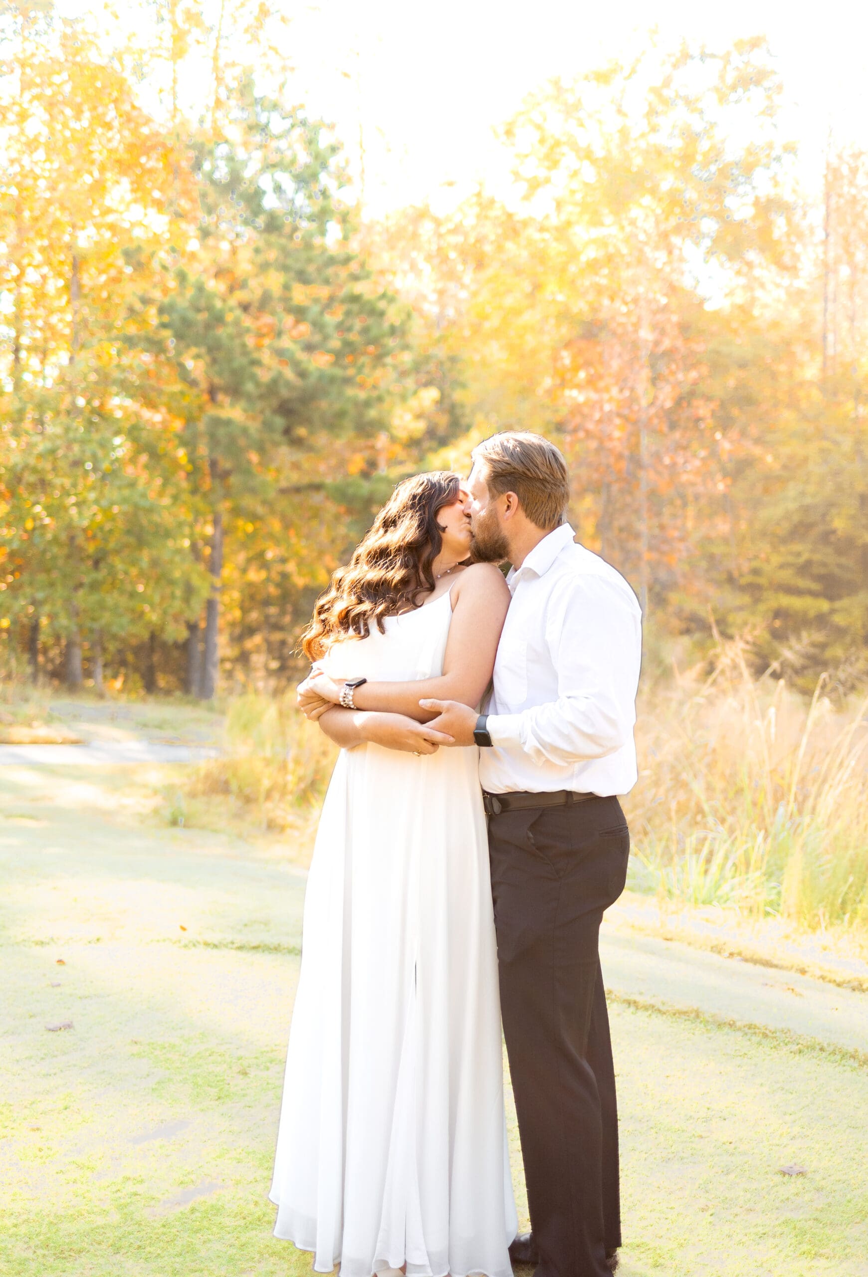 couple holding each other kissing on a putting green in front of forest