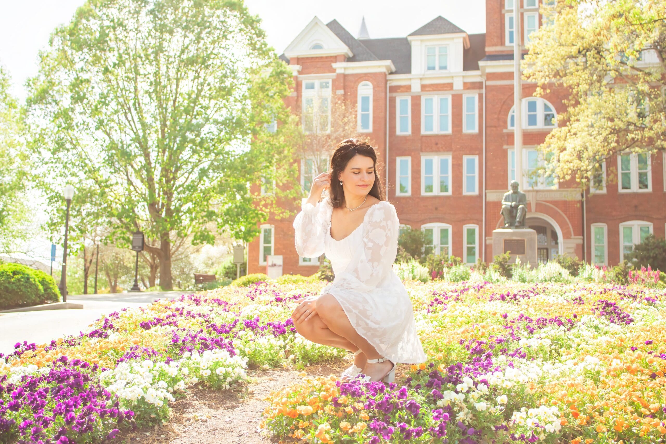 senior in front of Tillman Hall sitting in flower bed