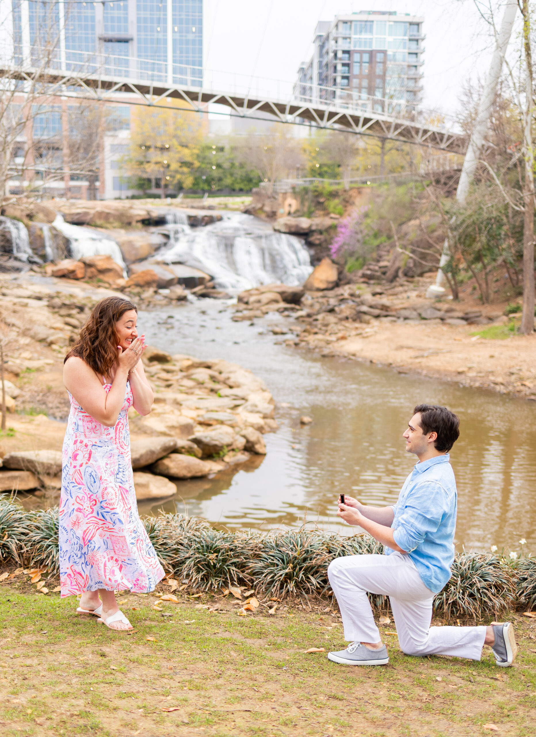 guy proposing on one knee in front of Falls Park river in Greenville with shocked girl