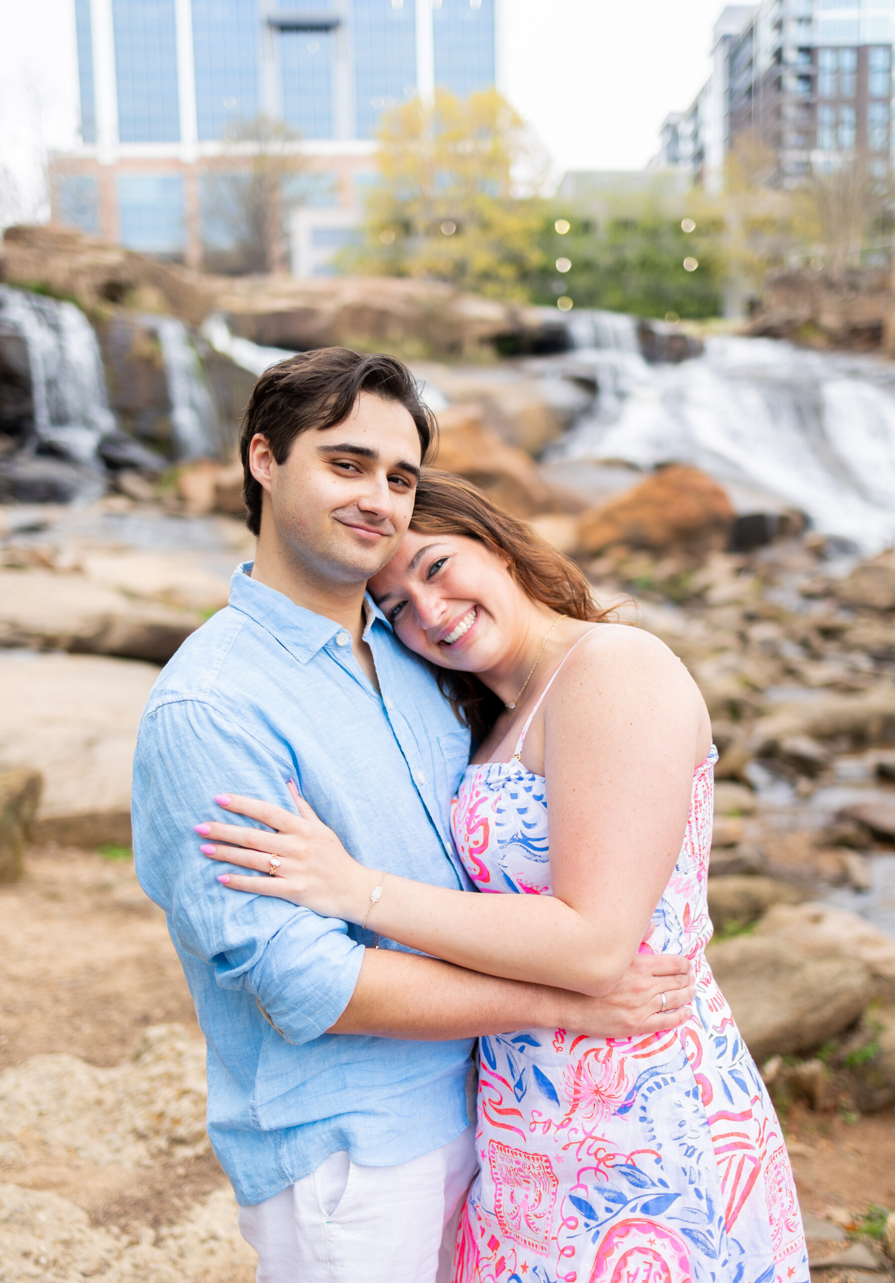 couple standing together on rocks in Falls Park river, resting heads on shoulders