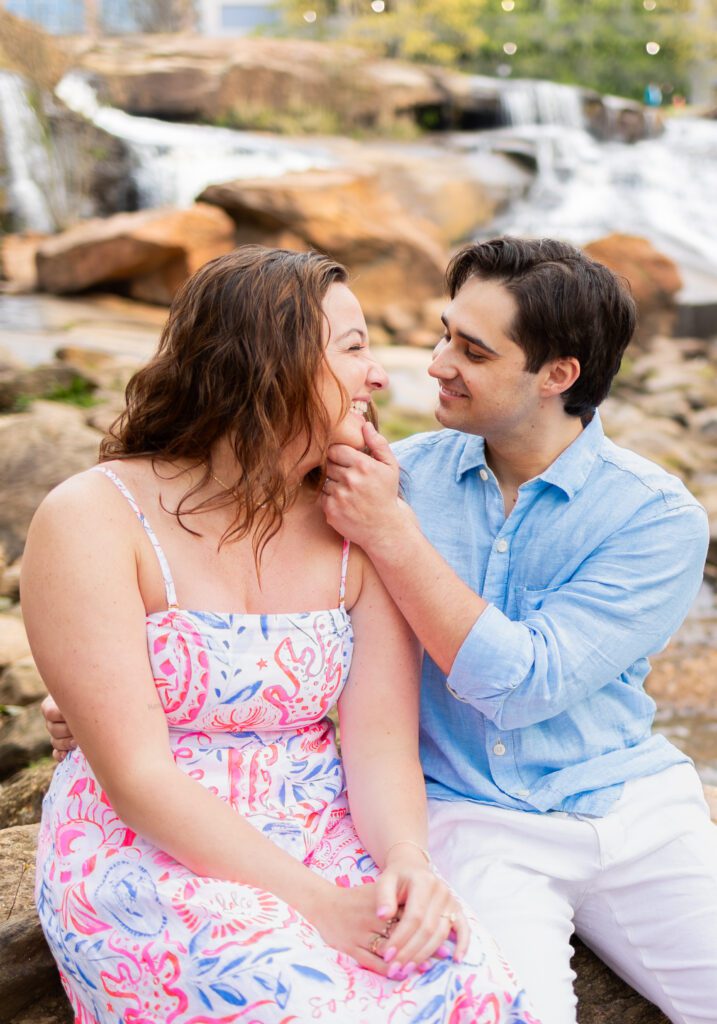 guy holding girls chin to look at each other lovingly, sitting on rocks in a river in greenville sc