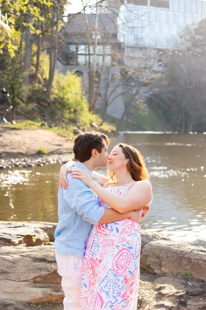 couple in front of river in greenville, holding each other, touching noses
