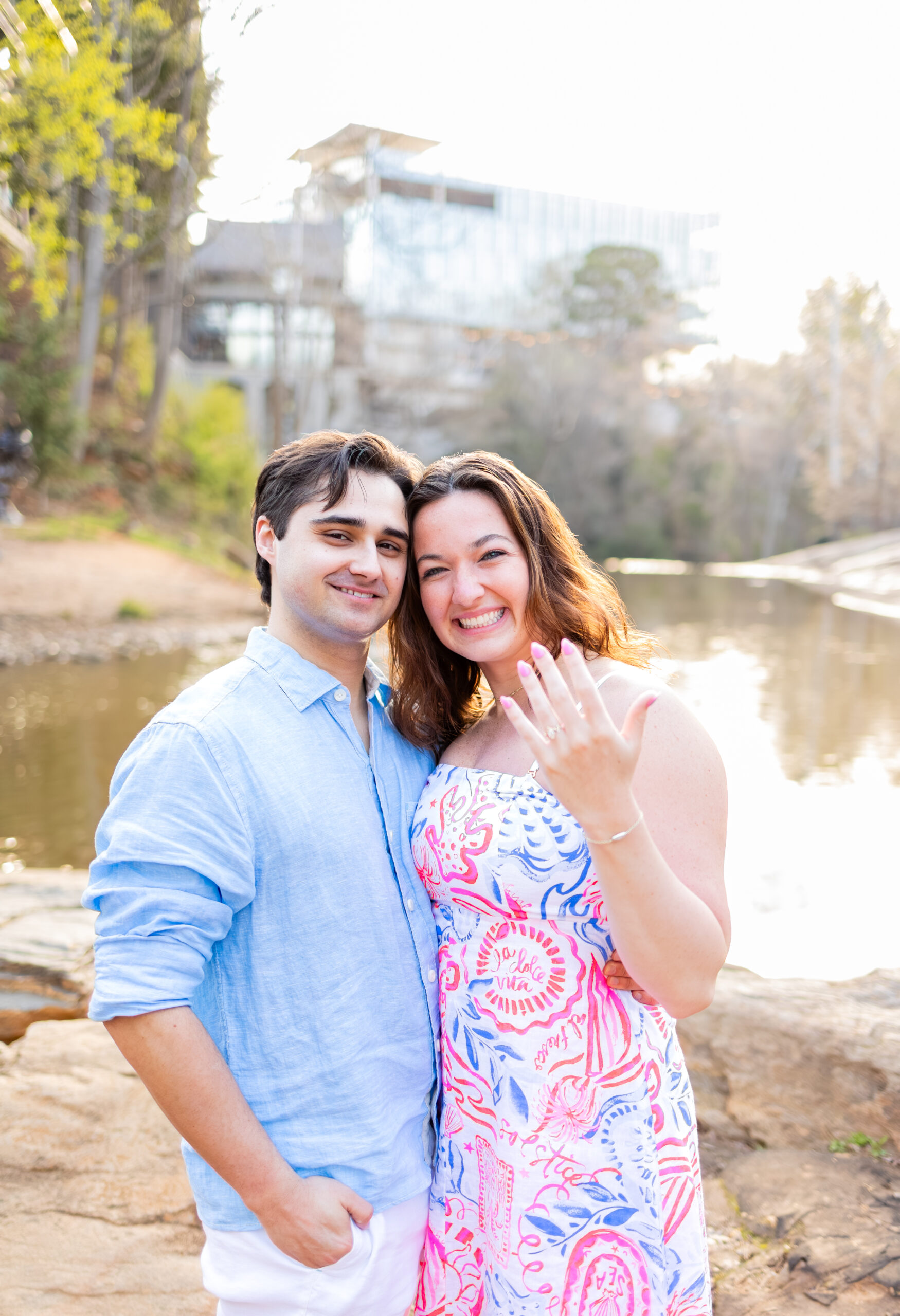 couple smiling together with girl showing off new engagement ring after proposal in Falls Park on the Reedy in Greenville